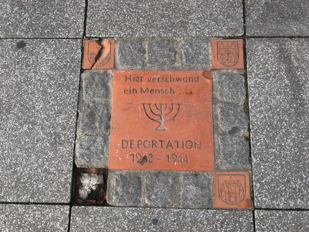 Gedenkpklatte, in den Gehweg eingelassen, mit dem Text: "Hier verschwand ein Mensch ... Deportation 1942 - 1944